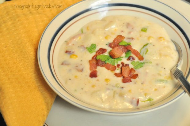 Corn bacon potato chowder is served with garnishes in bowl.