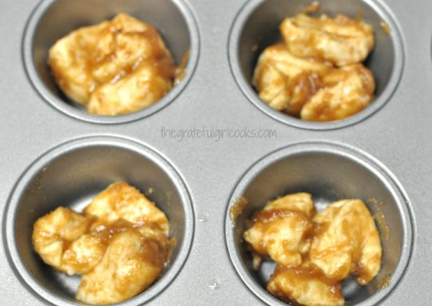 Three pieces of monkey bread minis dough is placed in each of 4 muffin tins.