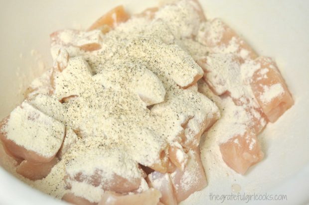 Chicken breast cubes are coated with flour and seasoning before cooking.