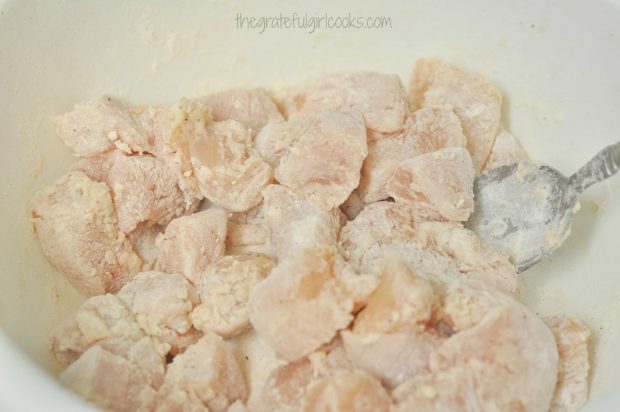 Excess flour is shaken off chicken breast cubes before cooking.