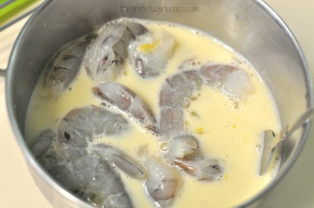 Shrimp rest in a bowl in a milk/egg mixture before coating in flour