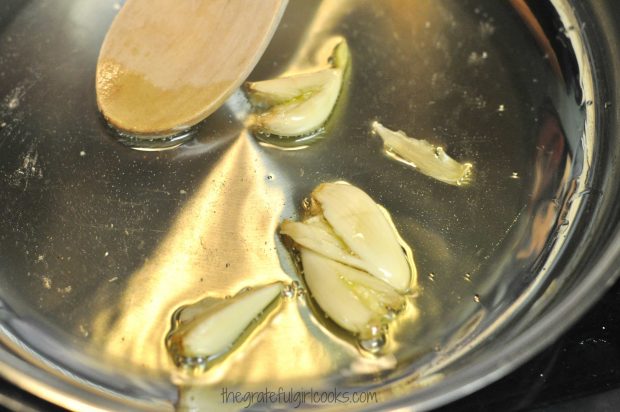 Cooking garlic cloves in olive oil to infuse flavor