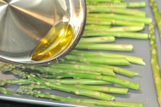 Garlic infused olive oil is poured over fresh asparagus