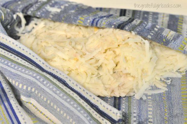 Grated potatoes are pressed in a dish towel to remove extra moisture.