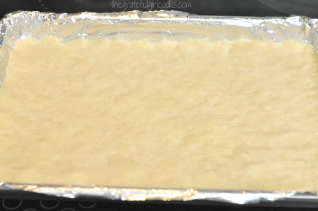 Shortbread crust for chocolate pecan pie bars is patted down to form crust.