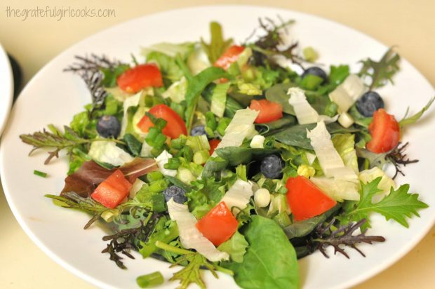 Mixed greens blueberries, green onions and tomatoes are placed in serving bowls.
