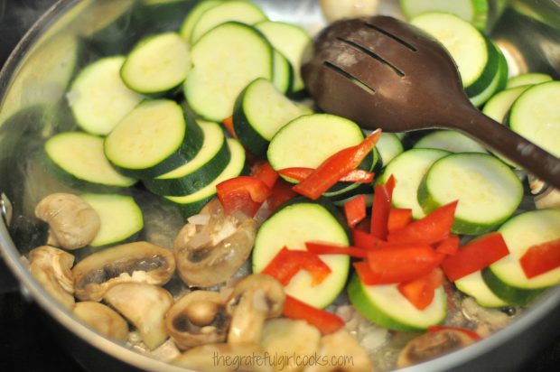 Sliced zucchini and red peppers are added to the mushrooms in the skillet.