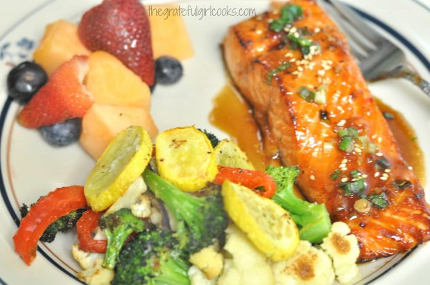 The salmon is served with fruit salad and roasted vegetables.