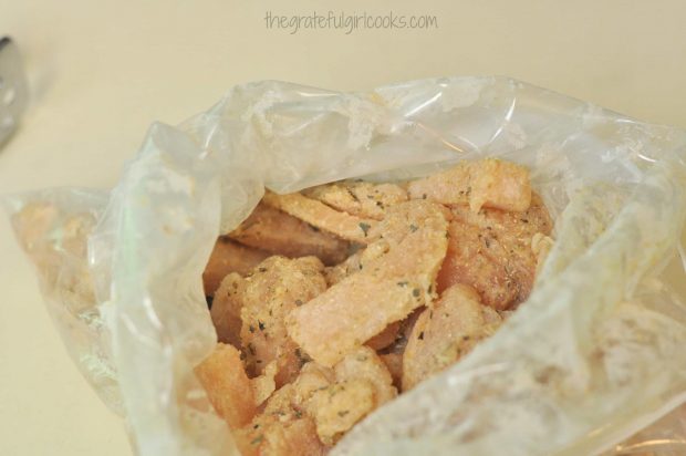Chicken slices are coated with flour and spices in a large plastic bag.
