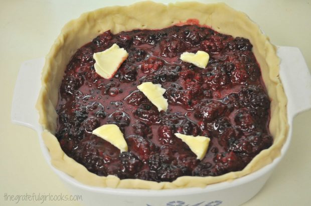 Butter chunks are placed on top of boysenberry pie filling.