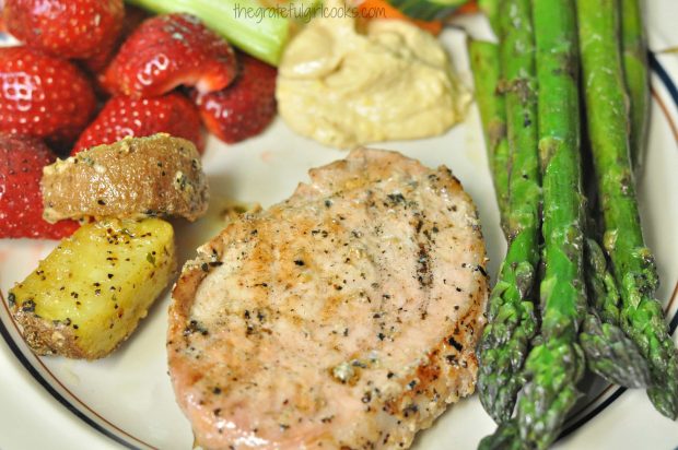 Marinated grilled pork chops are served with fruit, asparagus, and potatoes.