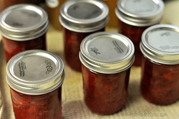 Jars of rhubarb-orange jam cooling on a dish towel, after processing.