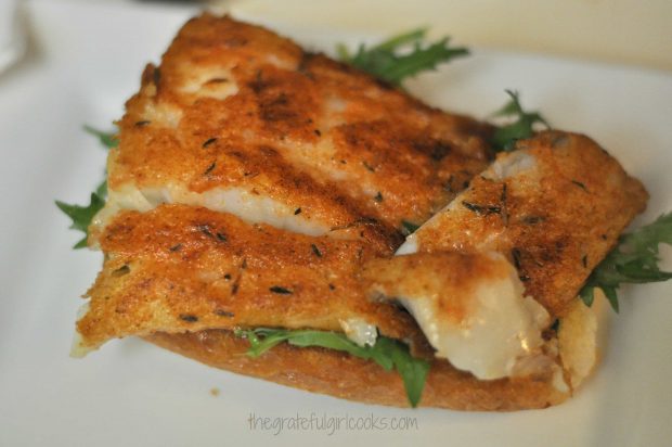 Arugula and pan-seared fish are placed onto sandwich roll.