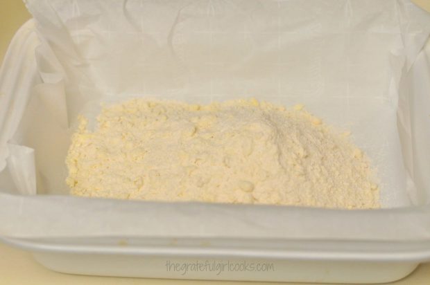 The processed crust mixture is placed in a parchment paper-lined baking dish.