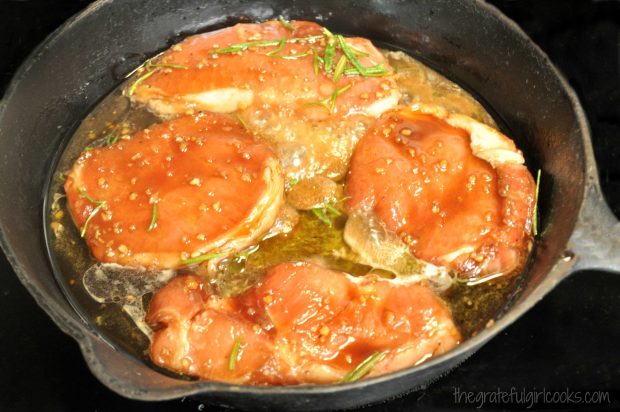 Four boneless pork chops cooking in a black cast iron skillet