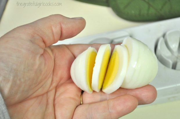 Hand holding a sliced hard boiled egg for topping the potato salad.