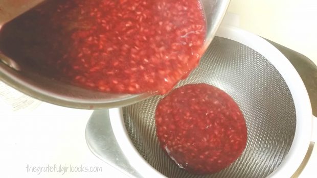 Cooked coulis is poured into a strainer which sits on top of bowl.