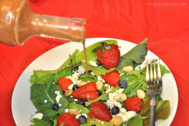 Pouring strawberry balsamic vinaigrette over salad, with strawberries and blueberries.