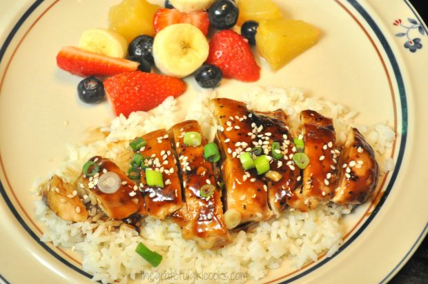 The teriyaki chicken is sliced and served on rice, with fruit on side.