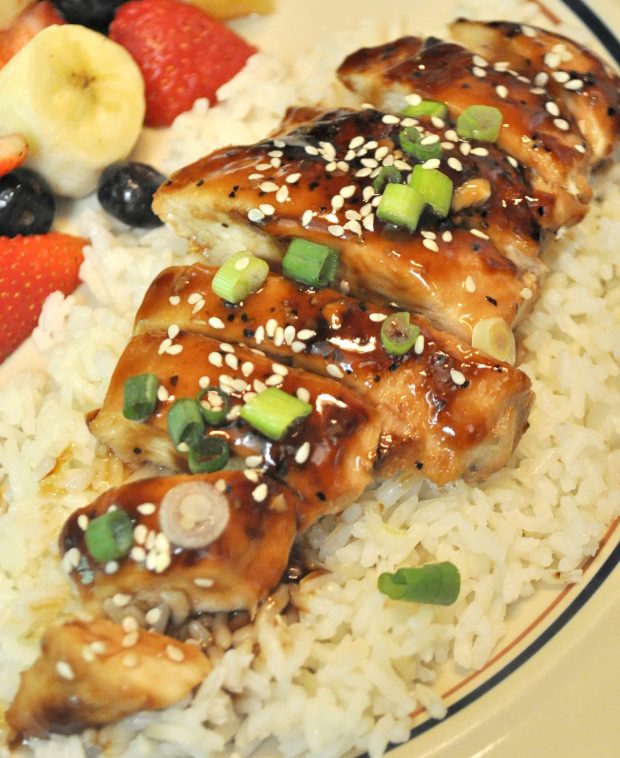 A serving of teriyaki chicken with sliced green onions, on top of white rice.