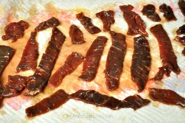 Marinated beef jerky strips draining on paper towel.