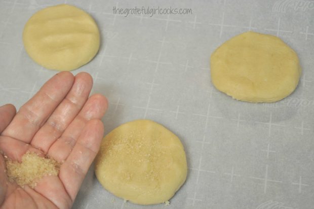 Giant sugar cookies are pressed down, then sprinkled with sugar before baking.