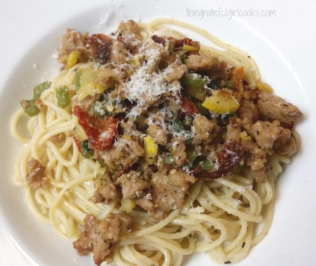 The finished pasta with Italian sausage is sprinkled with Parmesan and served in a white bowl.