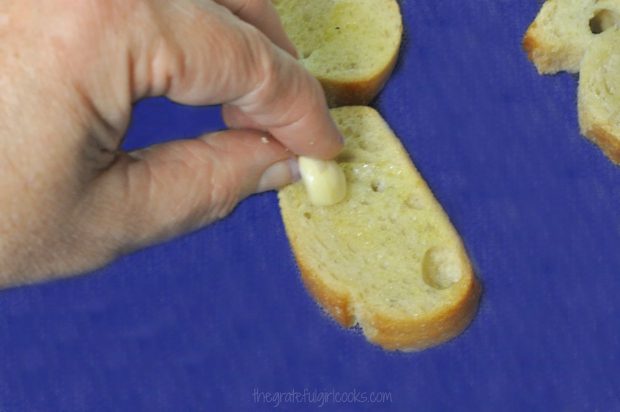 A fresh garlic clove is rubbed over baguette slices before baking.