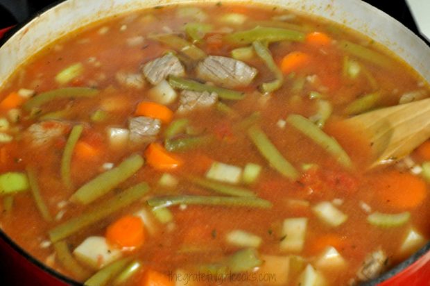 Water, green beans and bouillon added to beef stew in pan.