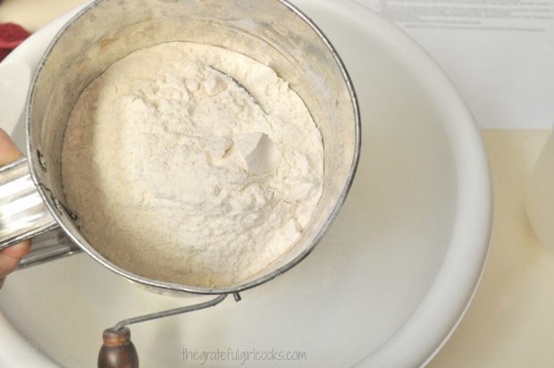 Flour for biscuits in sifter over a white bowl