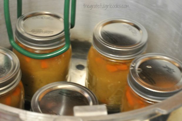 Split pea and ham soup jars are finished processing and are lifted out of canner with tongs.