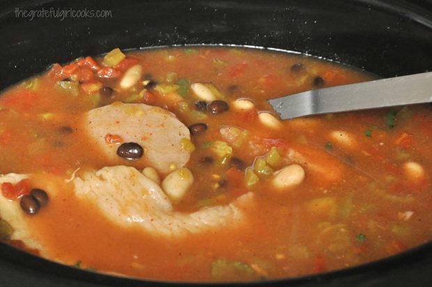 The chicken crockpot enchilada soup is cooked for several hours to tenderize the chicken.