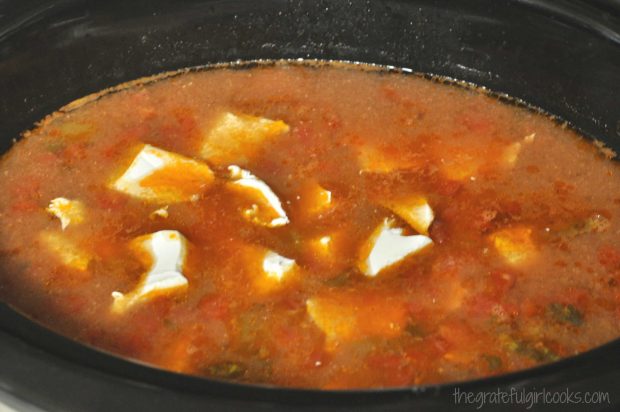 Cream cheese chunks are added to the hot chicken crockpot enchilada soup, to melt.
