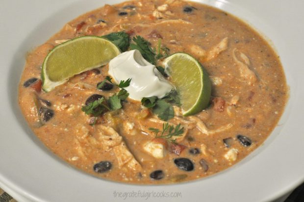 Green Chile Chicken Crockpot Enchilada Soup is garnished with sour cream, lime wedges and cilantro to serve.