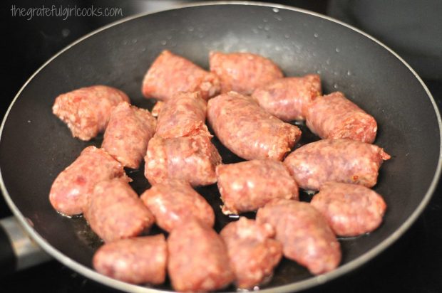 Italian sausage pieces brown in olive oil in a skillet.