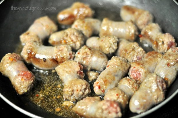 Browned Italian sausage slices, cooking in skillet.