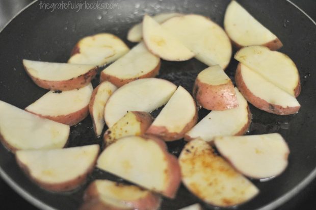 Sliced red potatoes are cooked in olive oil in skillet.
