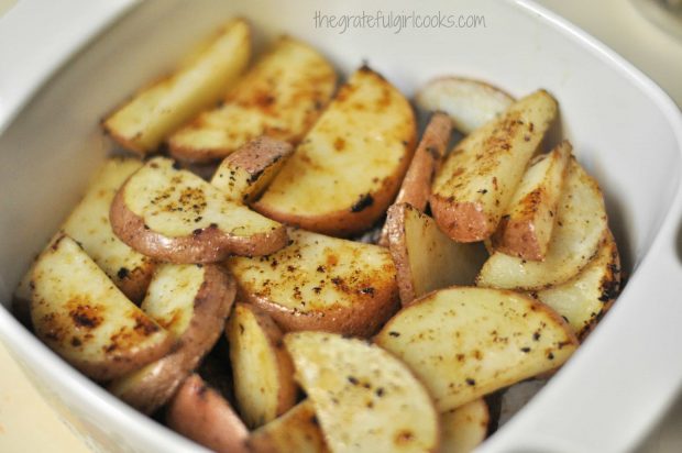 Cooked red potato slices are placed on top of Italian sausage in baking dish.