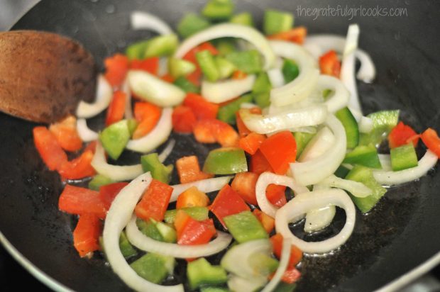 Onion slices and red and green peppers are cooked in skillet.