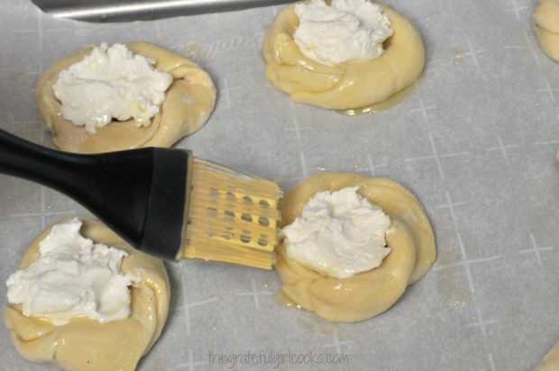 Brushing the danish pastries with melted butter before baking.