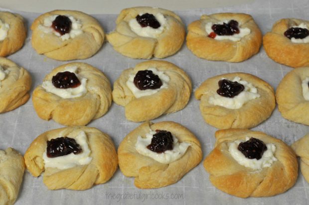 A dollop of raspberry jam is added to each baked danish pastry.