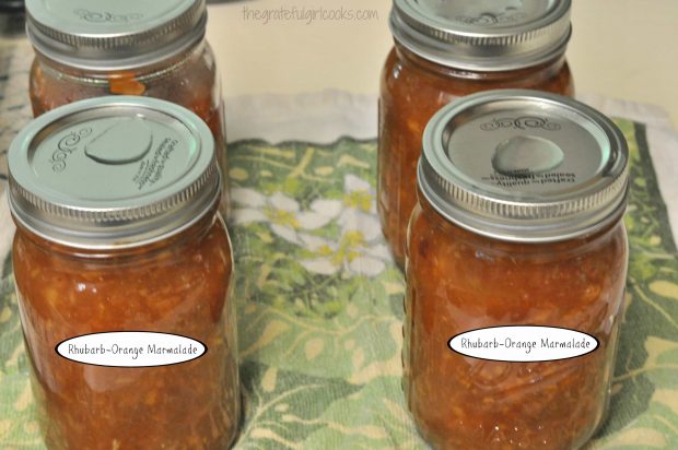 Jars of rhubarb-orange marmalade on dish towel after processing.