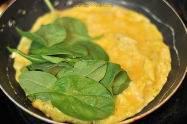 Raw spinach added to omelette in skillet