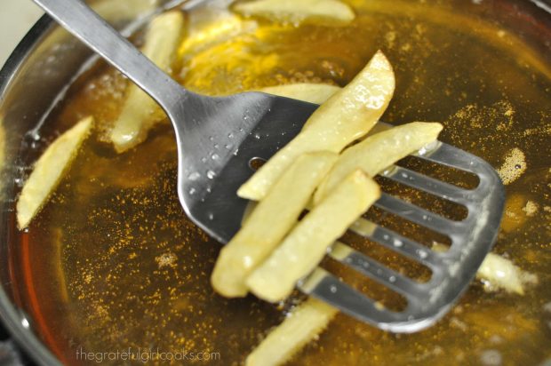 Homemade french fries are removed from hot oil with slotted spoon.