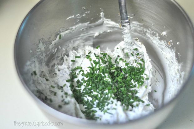 Fresh chopped chives are added to homemade boursin cheese in bowl.