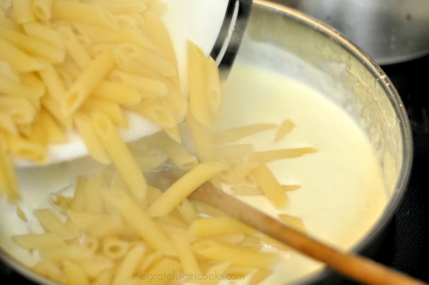 Hot, cooked pasta is added to sauce for Shrimp Penne Pasta Alfredo.