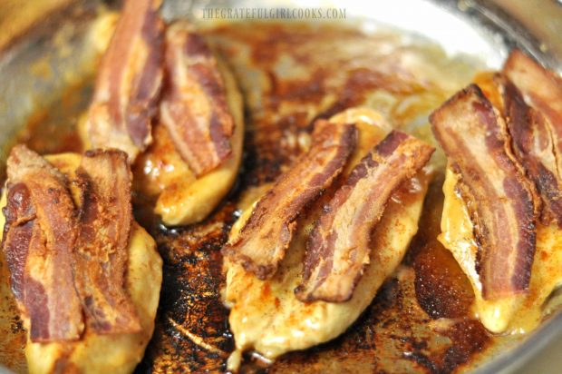 Bacon strips on top of cooked chicken breasts in skillet