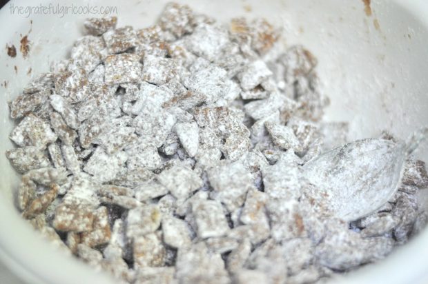 Chocolate Peanut Butter Muddy Buddies are coated with powdered sugar in bowl.