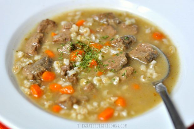 Beef and Barley Soup with barley, meat, carrots and broth in white bowl with spoon.