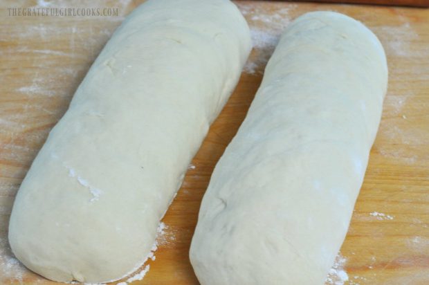 Two loaves of homemade white bread dough on wood cutting board